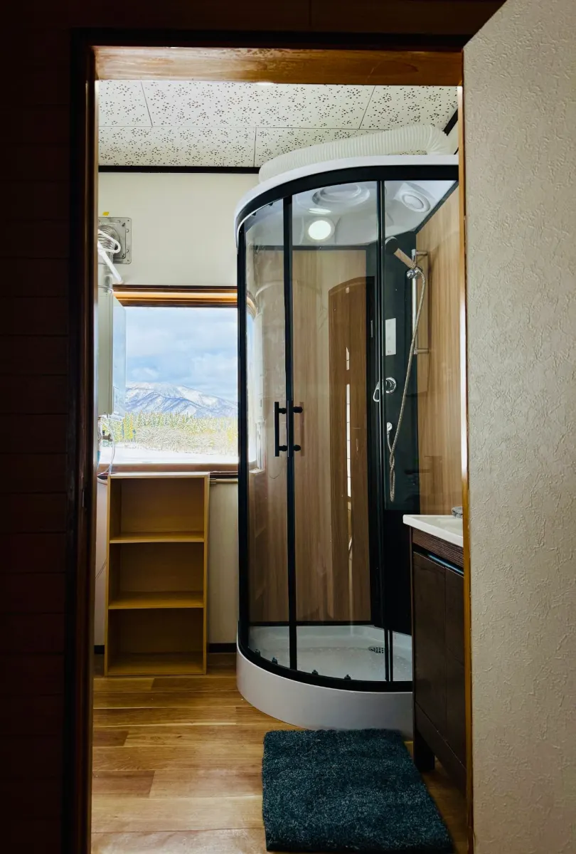 A second shower room with a glass shower cubicle and a basin, a window onto the mountains behind.