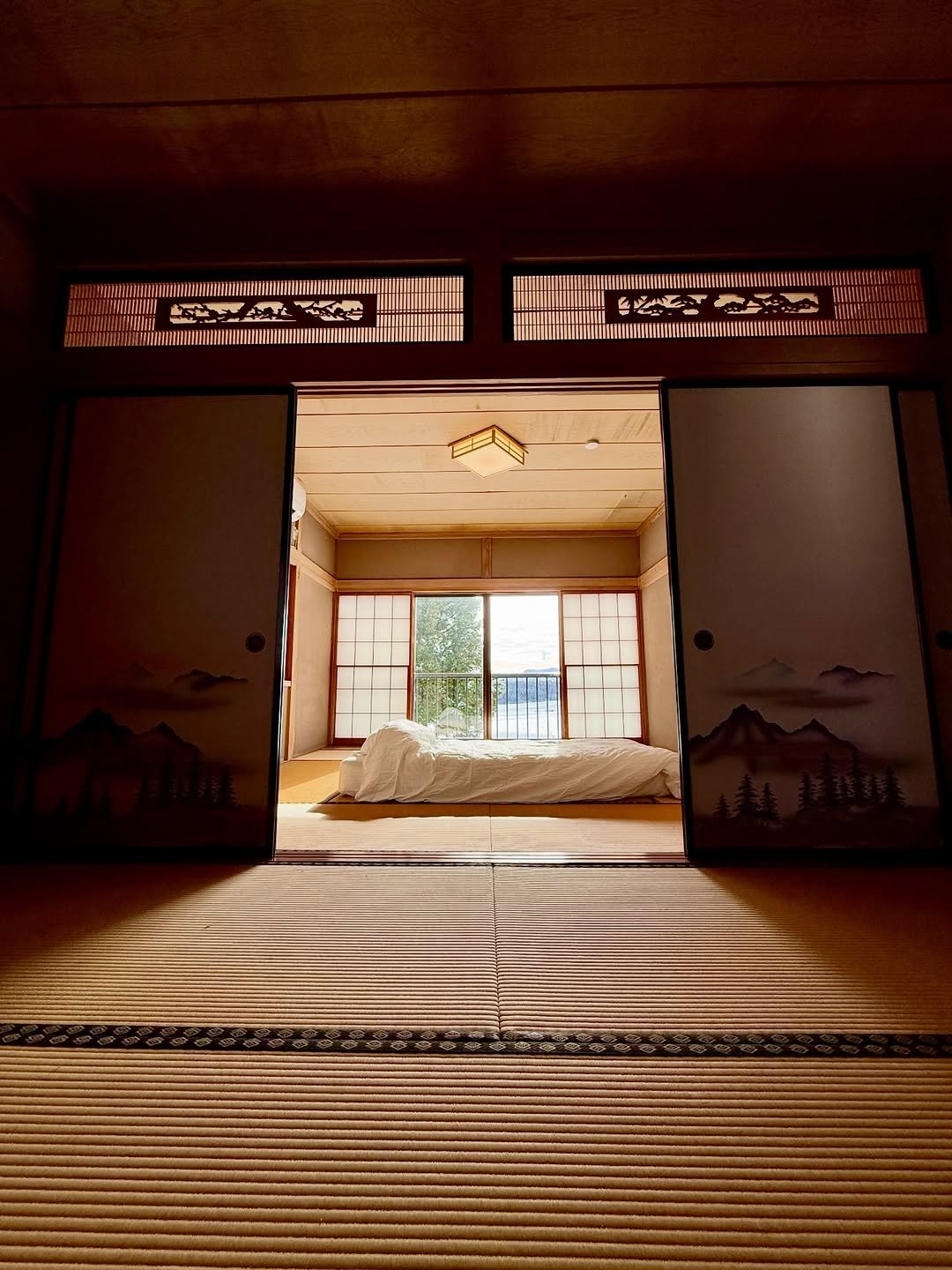 A tatami room seen through open sliding doors, futon laid out beneath a window onto the mountains.