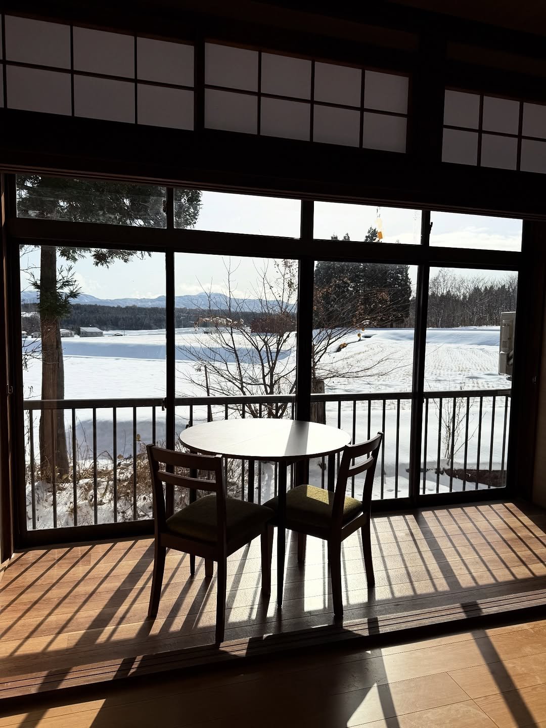 A small table by the window, low winter sun across the floorboards and snow-covered fields beyond.